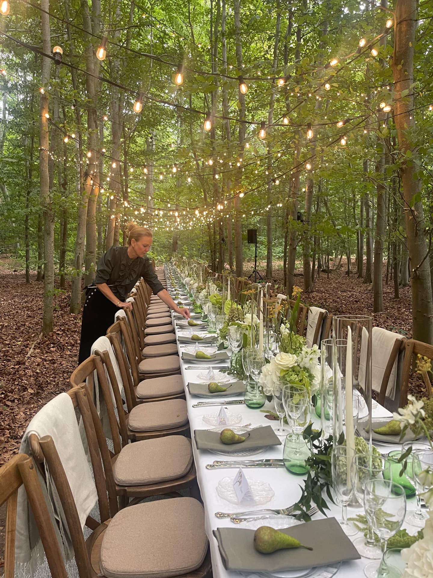 Christel Winther arranging a long wedding table in a woodland setting