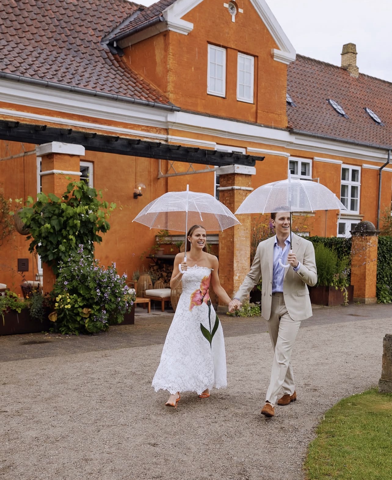 A newly married couple walking hand in hand with clear umbrellas in summer rain at a Danish manor
