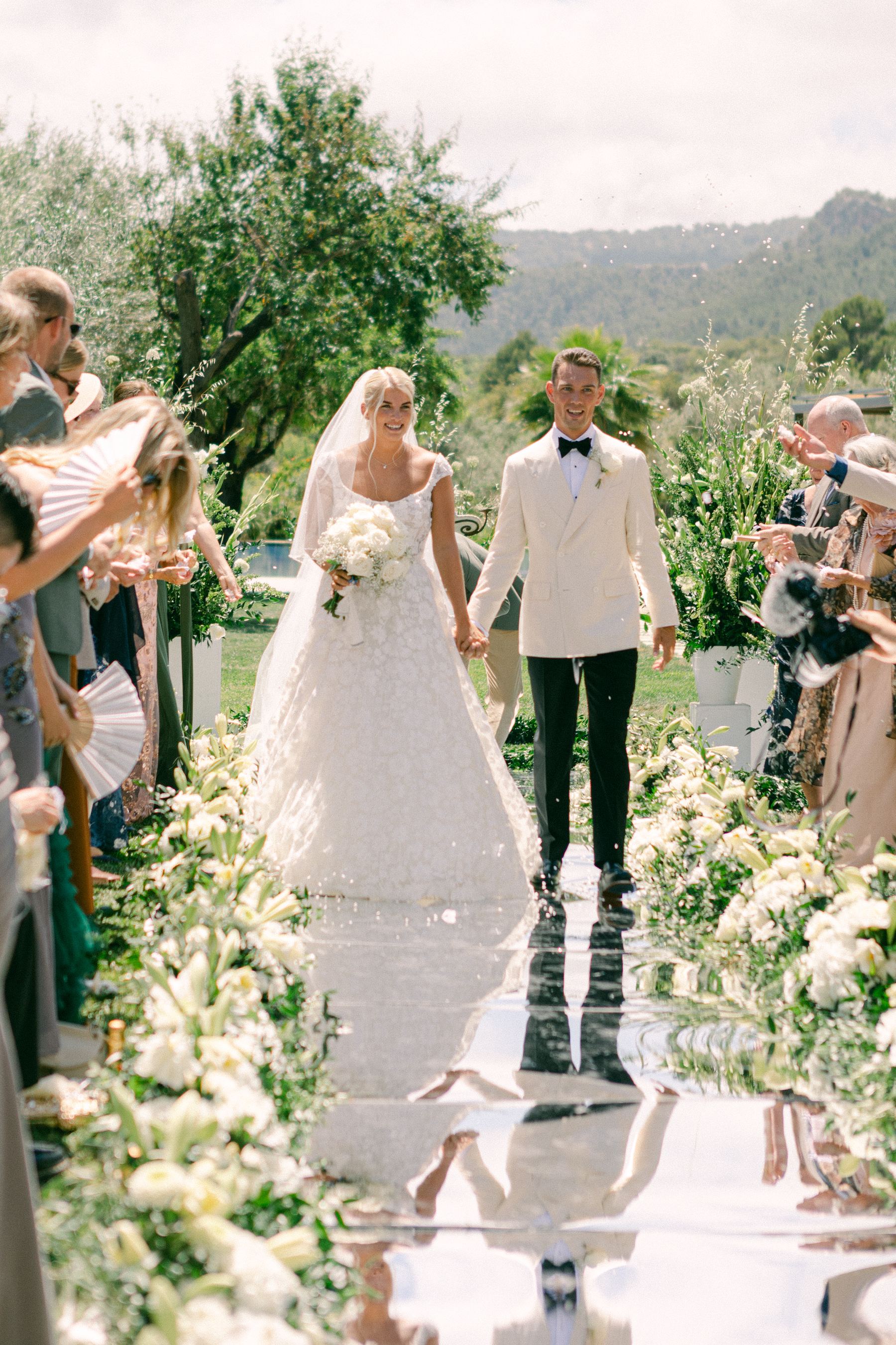 Bride and groom walking down a mirrored aisle surrounded by flowers