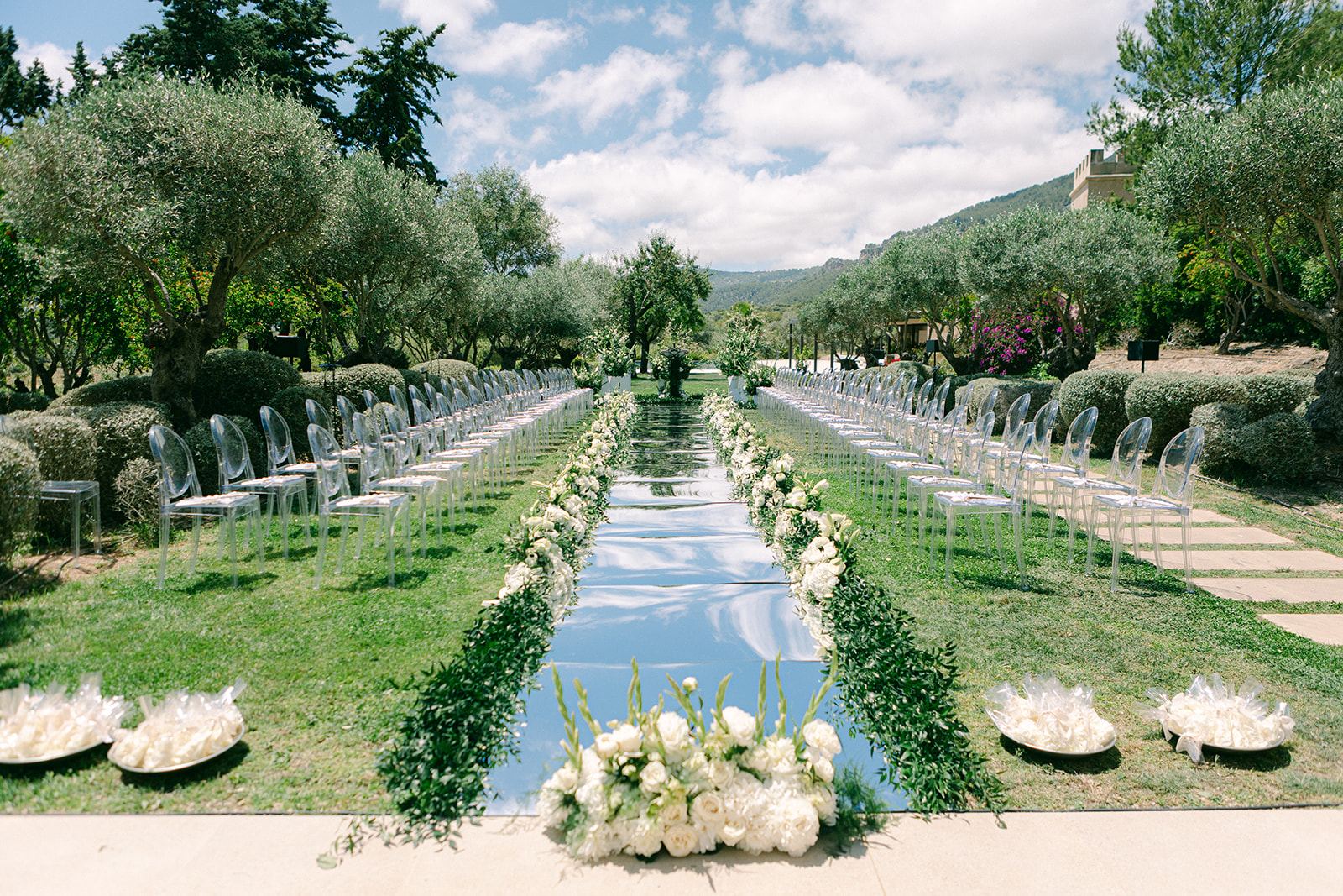Outdoor ceremony aisle with mirrored walkway, white roses and ghost chairs in Mallorca